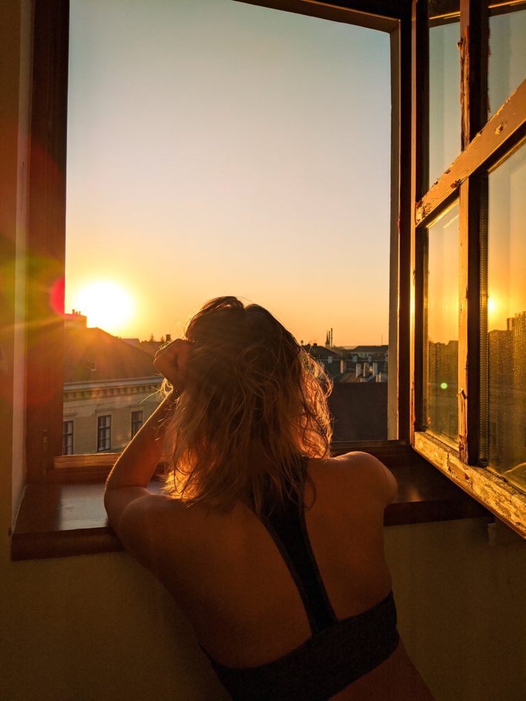 femme pensive, appuyée à sa fenêtre ouverte face au coucher de soleil