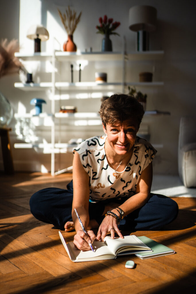 Cécile Routier Liot, coach professionnel diplômée, assise par terre, prenant des notes, sourire aux lèvres, regard vers l'avant